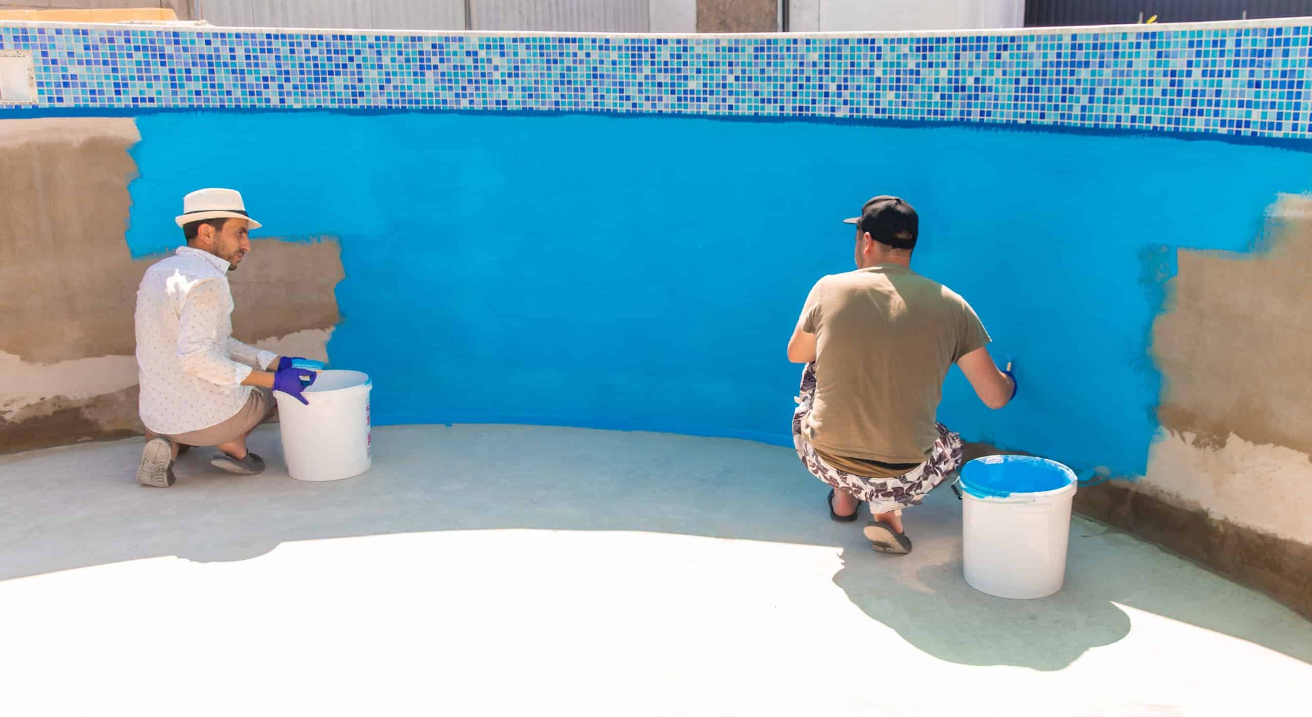 Two workers applying blue plaster to a swimming pool wall.