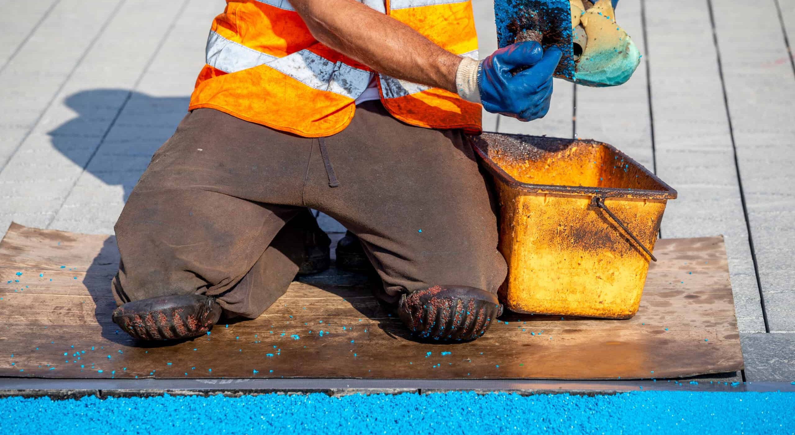 Worker applying waterproofing coating on pool deck surface.